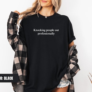 May include: Black t-shirt with the text "Knocking people out professionally" printed on the front.