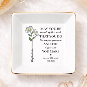 May include: A square, white ceramic trinket dish with a gold rim. The dish features a floral design and the text "MAY YOU BE proud of the work THAT YOU DO the person you are AND THE difference YOU MAKE Happy Retirement EST. 2026".