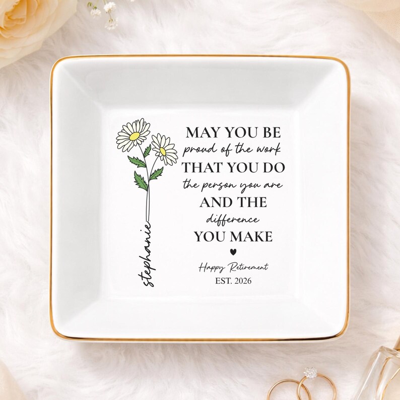 May include: A square, white ceramic trinket dish with a gold rim. The dish features a floral design and the text "MAY YOU BE proud of the work THAT YOU DO the person you are AND THE difference YOU MAKE Happy Retirement EST. 2026".
