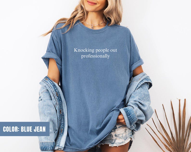 May include: A blue jean t-shirt with the text "Knocking people out professionally" printed on the front.