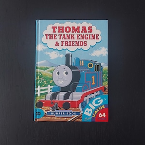 May include: A children's book titled "Thomas the Tank Engine & Friends." The cover shows a blue train with the number 1, set against a backdrop of green hills and a blue sky. The book is a "Bumper Book" with 64 pages.