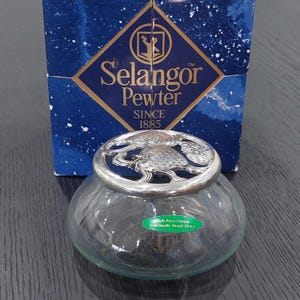 May include: A clear glass jar with a silver lid featuring a detailed design. The jar is presented with a blue box displaying "Selangor Pewter" and "Since 1885". A green sticker on the jar reads "Each Piece Unique Individually Mouth Blown".