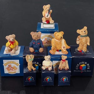 May include: A selection of miniature teddy bear figurines, each in a unique pose and presented on small blue boxes. The bears are various shades of brown and tan, some wearing accessories like a banjo, scarf, or overalls. The boxes have the text "TEDDY BEAR COLLECTION" and "COLOUR-BOX miniatures".