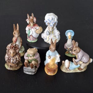 May include: A collection of eight hand-painted ceramic animal figurines featuring rabbits, a hedgehog, a frog, and a duck. The figures are depicted in various poses, wearing detailed clothing, and include accessories like baskets, bowls, and books.