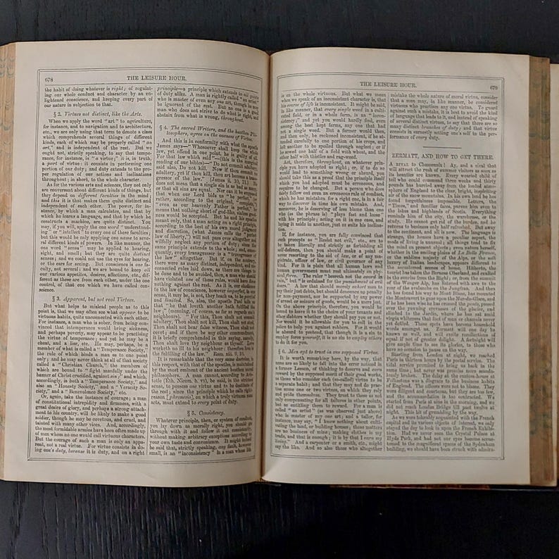 May include: An open book with aged, yellowed pages. The text is small and densely packed, with a title at the top of each page. The book is open on a dark surface, suggesting a vintage or antique item.