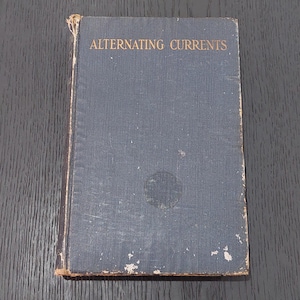 以下が含まれることがあります： 「ALTERNATING CURRENTS」のタイトルが金色の文字で記された、濃い青色の表紙の古書。表紙には擦り切れや変色が見られる。古書であり、アンティーク品である可能性が高い。