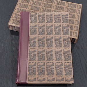 May include: A hardcover book and matching box. The book has a burgundy spine and a patterned cover in shades of brown and gray. The box has the same pattern. The pattern appears to be a stylized landscape.