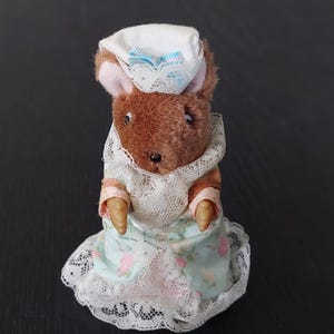 May include: A brown plush mouse wearing a white and blue hat with a lace trim and a light blue dress with a white lace trim and pink flowers.
