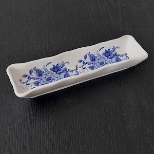 May include: A white ceramic serving dish with a blue floral design. The dish has a wavy edge and is perfect for serving snacks or appetizers.