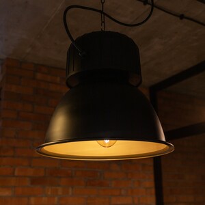 May include: A black industrial-style pendant light with a large, round shade and a single light bulb. The light is hanging from a chain and is suspended from a ceiling.