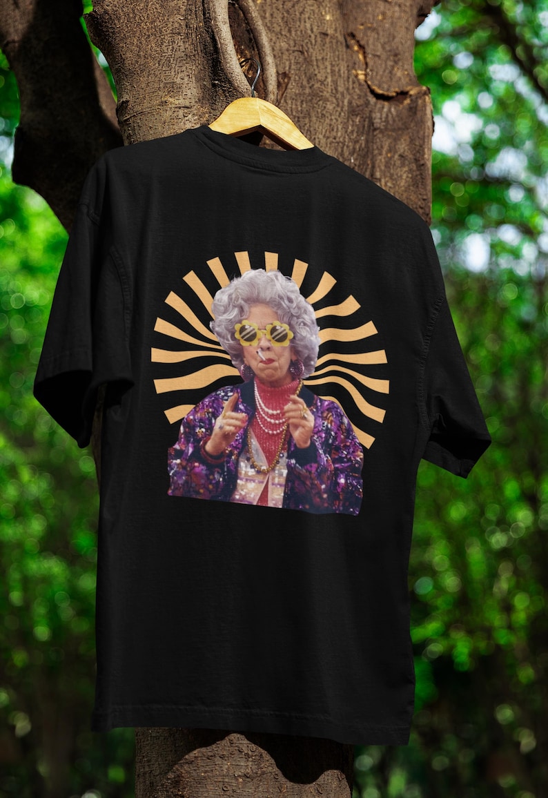 May include: Black t-shirt with a graphic print of a woman wearing sunglasses and a sequined jacket. The graphic is surrounded by a gold sunburst design.