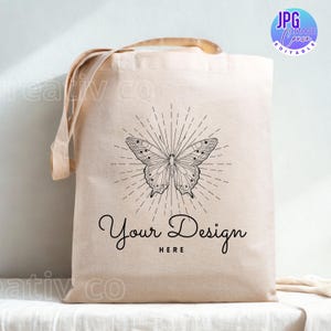 May include: Beige canvas tote bag with a butterfly design and the text "Your Design Here". The butterfly is black and white with radiating lines. The bag has long handles for carrying.