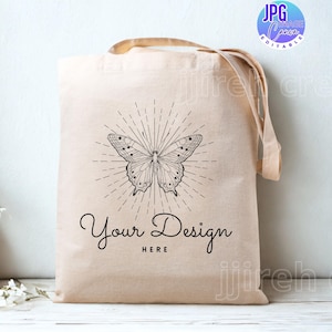 May include: Beige tote bag featuring a black butterfly design and the text "Your Design HERE". The butterfly has detailed wing patterns and is surrounded by radiating lines. The bag has tan handles.