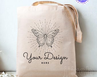 Op de afbeelding: Beige draagtas met een zwart vlinderontwerp en de tekst "Your Design HERE". De vlinder heeft gedetailleerde vleugelpatronen en is omgeven door stralende lijnen. De tas heeft bruine handvatten.