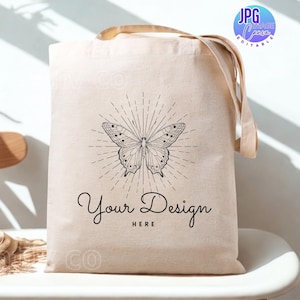 May include: A beige canvas tote bag featuring a black butterfly design and the text "Your Design HERE". The bag has tan handles and is on a white surface. The image also includes a "JPG Image Canva Editable" logo.