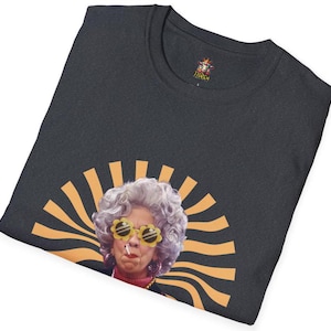 May include: A dark gray t-shirt with a graphic of a woman with gray hair wearing yellow sunglasses and a cigarette. The graphic is surrounded by orange and yellow sun rays.
