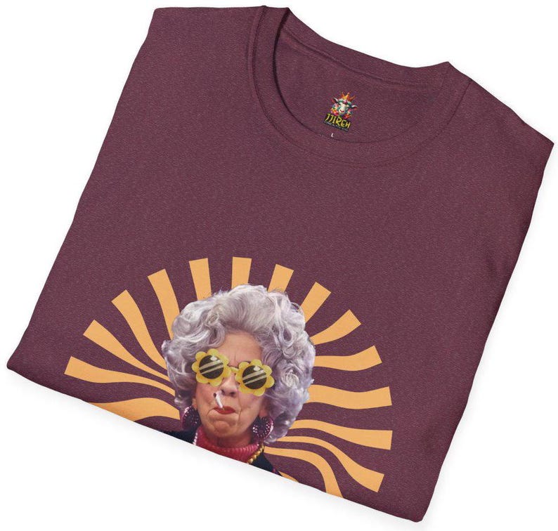 May include: A maroon t-shirt with a graphic of a woman with gray hair wearing yellow sunglasses and a cigarette. The woman is in front of a yellow and orange sunburst design.