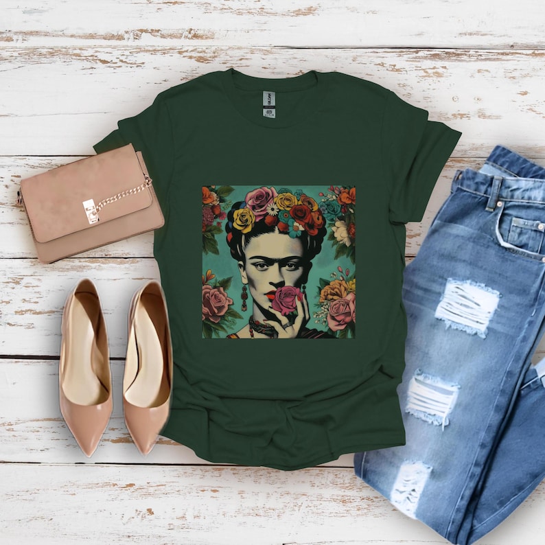 May include: A dark green t-shirt with a colorful graphic print of Frida Kahlo wearing a flower crown and holding a flower. The graphic is on a light blue background.