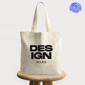 May include: A white canvas tote bag with black handles and the text "DESIGN HERE" printed in black bold letters.