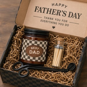 Op de afbeelding: Een Vaderdag cadeaupakket met een kaars, lucifers en een lontschaar. De kaars heeft een bruin en wit geblokt patroon en een ovaal label met de tekst "BEST DAD". De doos is gevoerd met bruin papier en heeft de tekst "HAPPY FATHER'S DAY".