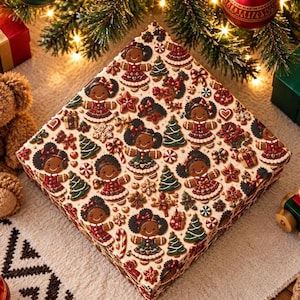 Op de afbeelding: Een vierkante geschenkdoos met een herhalend patroon van peperkoekfiguren met een donkere huidskleur, gekleed in rood-groene outfits, afgewisseld met kleine groene kerstbomen, rode sterren, zuurstokken en sneeuwvlokken op een crèmekleurige achtergrond.