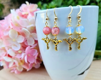May include: A pair of gold key earrings with pink and white opal beads. The keys have wings and hearts.
