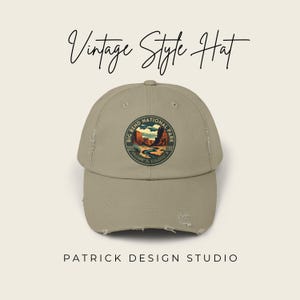 May include: A khaki-colored, distressed baseball cap with a circular patch featuring a landscape scene from Big Bend National Park. The text "Vintage Style Hat" is above the cap, and "Patrick Design Studio" is below.