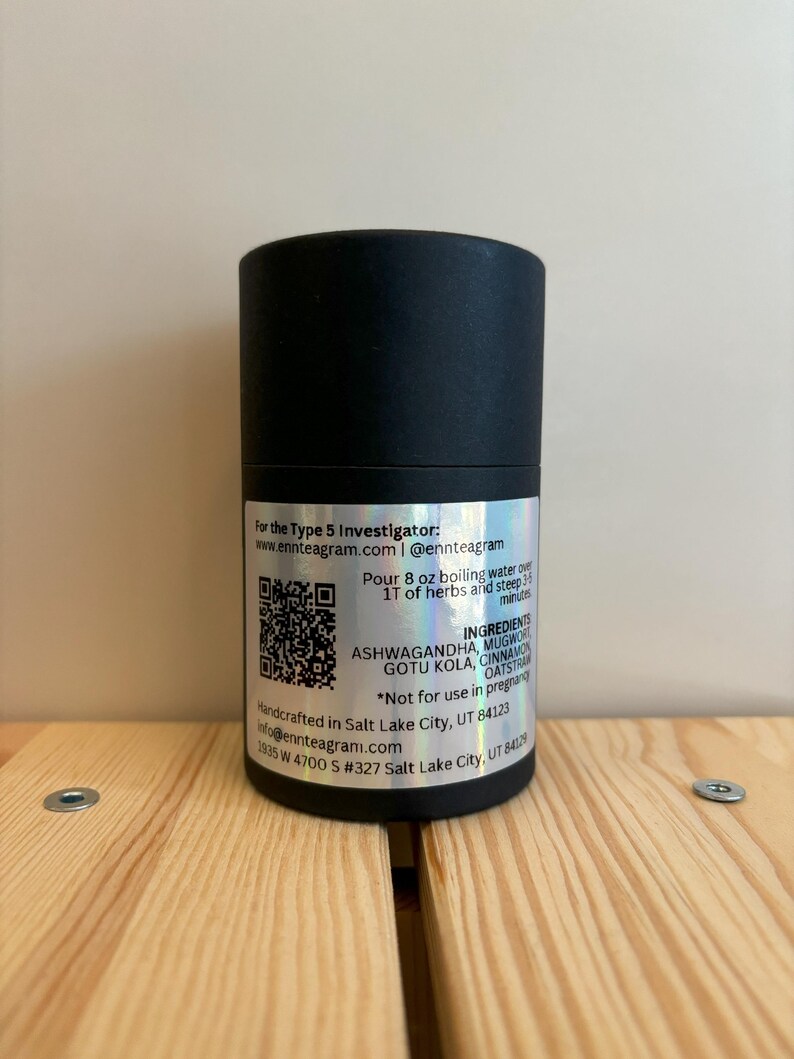 Puede incluir: Un recipiente cil&iacute;ndrico negro con una etiqueta plateada. La etiqueta incluye texto sobre los ingredientes, las instrucciones y el sitio web del producto. El recipiente est&aacute; sobre una superficie de madera.