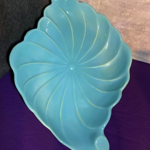 May include: A light blue ceramic serving bowl with a swirl design. The bowl is shaped like a seashell and has a smooth, glossy finish.