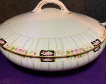 May include: White porcelain serving dish with a lid. The dish has a gold trim and a floral pattern with pink roses and green leaves. The lid has a gold knob.