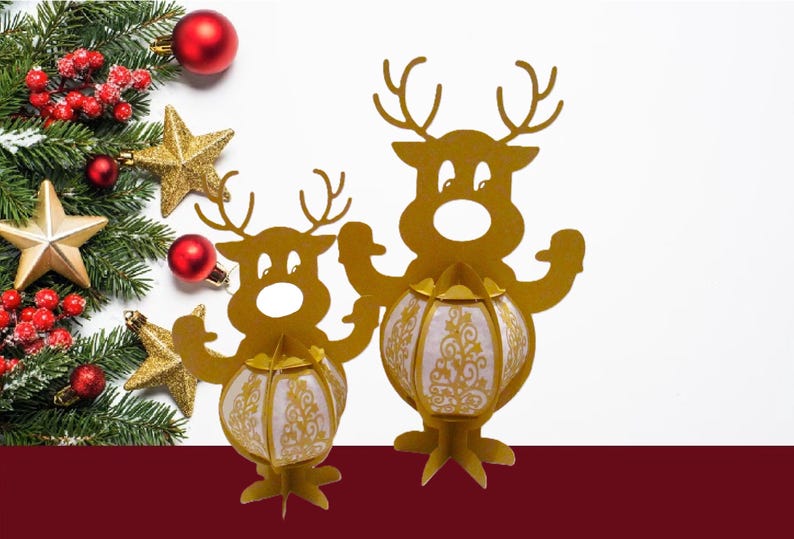 May include: Two gold-colored reindeer-shaped lanterns with white and gold patterned globes. The lanterns are on a white background with Christmas decorations, including a fir branch, red berries, gold stars, and red ornaments.