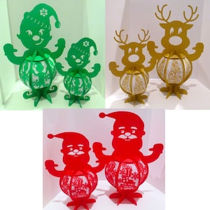 May include: A collection of Christmas decorations featuring paper cutouts of elves, reindeer, and Santa Claus. The elves are green, the reindeer are gold, and the Santa figures are red. Each figure has a decorative globe-shaped body with a snowflake or gift design.