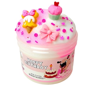 May include: A container of Slime Dazzle with a birthday theme. The slime is topped with pink frosting, sprinkles, and decorative elements like a cupcake, bow, and ice cream cone. The container has a label with the words "Happy Birthday" and a cartoon pug.