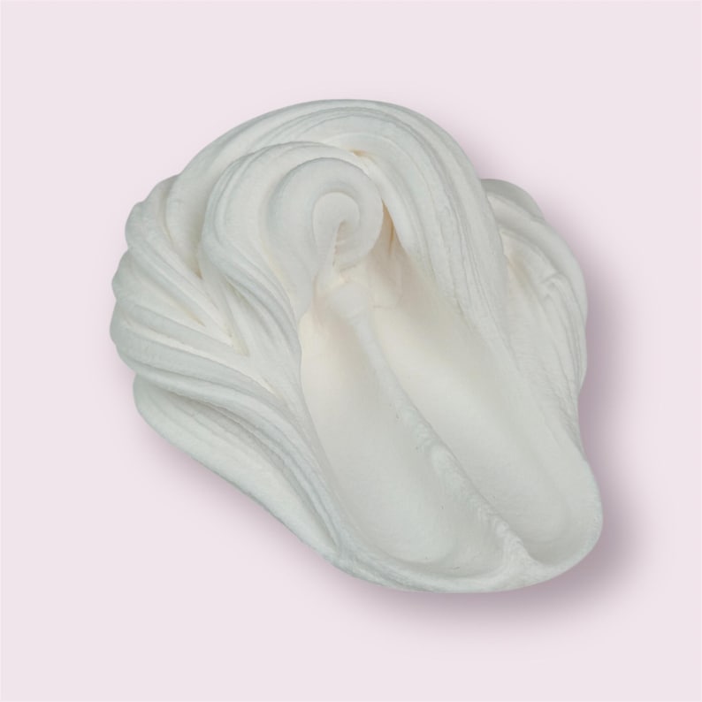 May include: A close-up shot of a swirl of white slime against a light pink background. The slime has a smooth, creamy texture with visible ridges and folds, creating a dynamic, textured appearance. The overall effect is soft and inviting.