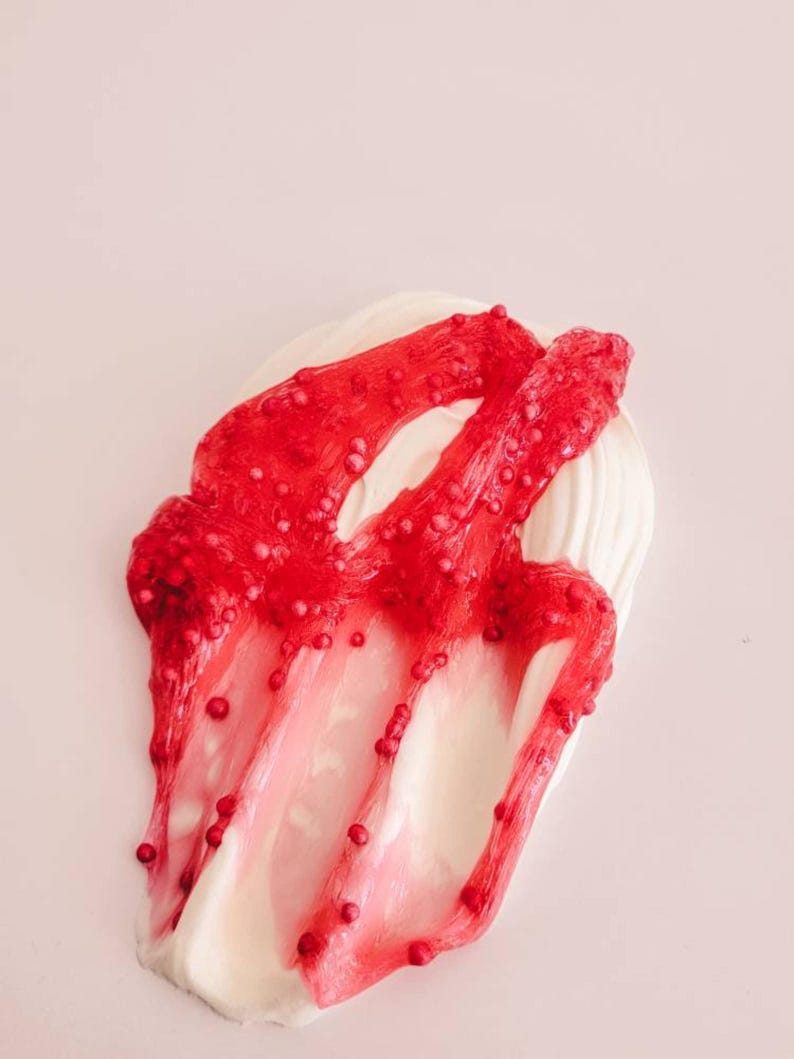 May include: A close-up of a white and red slime. The red slime is a translucent, jelly-like substance with small red beads throughout. The white slime is a thick, opaque base. The background is a light pink.