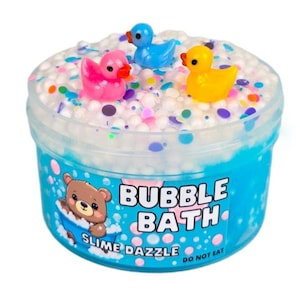 May include: A clear plastic container filled with blue slime with white foam and colorful sprinkles. The container has a label that says "Bubble Bath Slime Dazzle Do Not Eat" and features a cartoon bear in a bathtub. There are three small rubber duck toys on top of the slime.