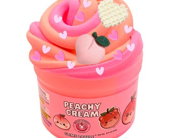 Może przedstawiać: Pojemnik ze slime Peachy Cream z wirującą masą o teksturze w kolorach różowym i pomarańczowym, ozdobiony zawieszką w kształcie brzoskwini, gofra w kształcie serca oraz małymi różowymi posypkami w kształcie serc. Etykieta zawiera napis Peachy Cream i Net Wt. 8 Fl Oz 227g.