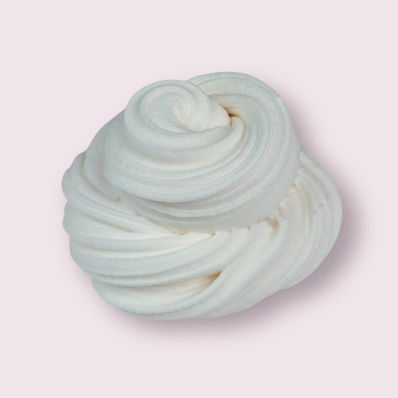 May include: A swirl of white slime against a light pink background. The slime has a soft, creamy texture with visible ridges and a slight off-white hue. The image is well-lit, highlighting the texture and form of the slime.