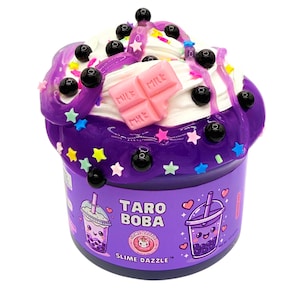 May include: A purple slime container labelled Taro Boba Slime Dazzle, topped with white cream, black boba beads, colourful star sprinkles, and a pink chocolate bar charm. The label features illustrations of two boba tea cups with faces.