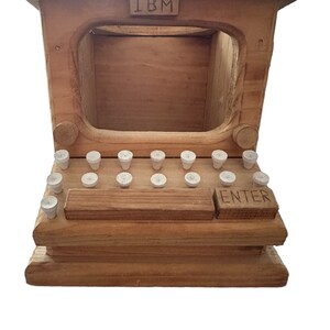 May include: A wooden toy computer with the word "IBM" on the top and a screen. The computer has a keyboard with white keys and an "ENTER" key.