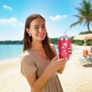 May include: A red insulated tumbler with a silver straw, featuring a white palm tree design and the name "Dahlia" with "San Diego 2023" printed below. The tumbler is held against a beach backdrop.