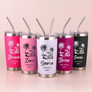 May include: Five stainless steel travel tumblers with silver straws. Each tumbler has a different color: pink, light pink, white, dark pink, and black. Each features a beach scene with palm trees and the name and year "San Diego 2026".