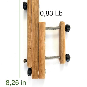 Wooden Mahlstick , light brown, 8.26 inches tall, 0.83 pounds.  Features two sets of parallel wooden blocks joined by a spring-loaded metal screw mechanism.  Black plastic knobs on each end.  A small metal pin is visible on the lower left side.  .