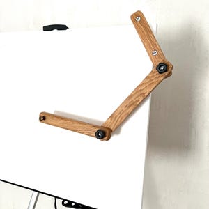 Close-up view of a wooden  Mahl stick . The Mahl stick is light brown, made of oak wood, and features a two-part articulated arm with black knobs for adjustment.