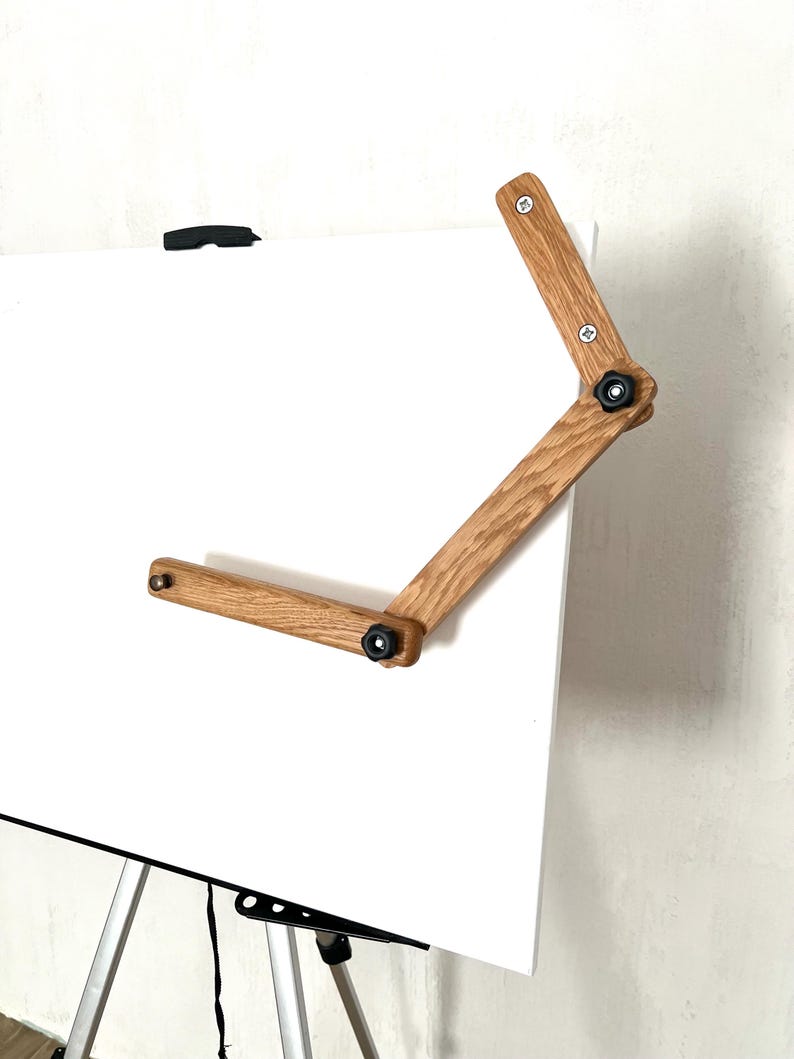 Close-up view of a wooden  Mahl stick . The Mahl stick is light brown, made of oak wood, and features a two-part articulated arm with black knobs for adjustment.