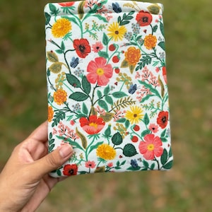 May include: A white fabric pouch with a floral print featuring red, yellow, and pink flowers, green leaves, and small blue butterflies.