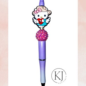 May include: A decorative pen with a Hello Kitty charm holding a heart. The pen has a purple and white ombre design, a pink jeweled sphere, and a black tip. The pen has the text "KJ Boutique" in a circle.