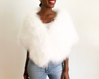 May include: White feather boa shawl with a soft, fluffy texture. The shawl is draped over the shoulders of a person wearing blue jeans.