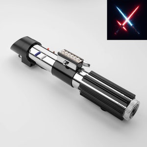 Puede incluir: Un sable de luz de r&eacute;plica con un mango negro y plateado, con un agarre acanalado y una serie de botones y luces. El dise&ntilde;o incluye un emisor plateado y una parte superior negra. Un gr&aacute;fico de sables de luz azules y rojos cruzados est&aacute; en la esquina.