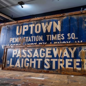 Puede incluir: Dos letreros vintage azules y blancos con marcos marrones. El letrero más grande dice "UPTOWN PENN STATION. TIMES SQ.". El letrero más pequeño dice "PASSAGEWAY TO LAIGHT STREET."